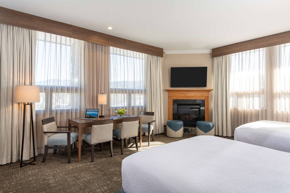 Une chambre d’hôtel avec deux lits, un bureau avec un ordinateur portable, des chaises, une télévision et une cheminée.