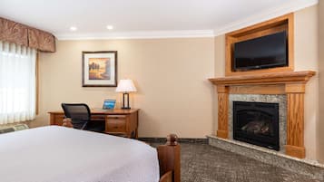 Una habitación de hotel con una cama grande, un escritorio con una computadora portátil, un televisor sobre la chimenea y un cuadro en la pared.