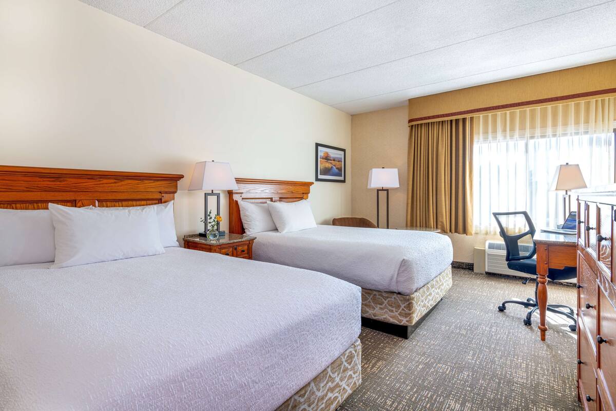 Une chambre d’hôtel avec deux lits, un bureau, une chaise et une fenêtre avec des rideaux.