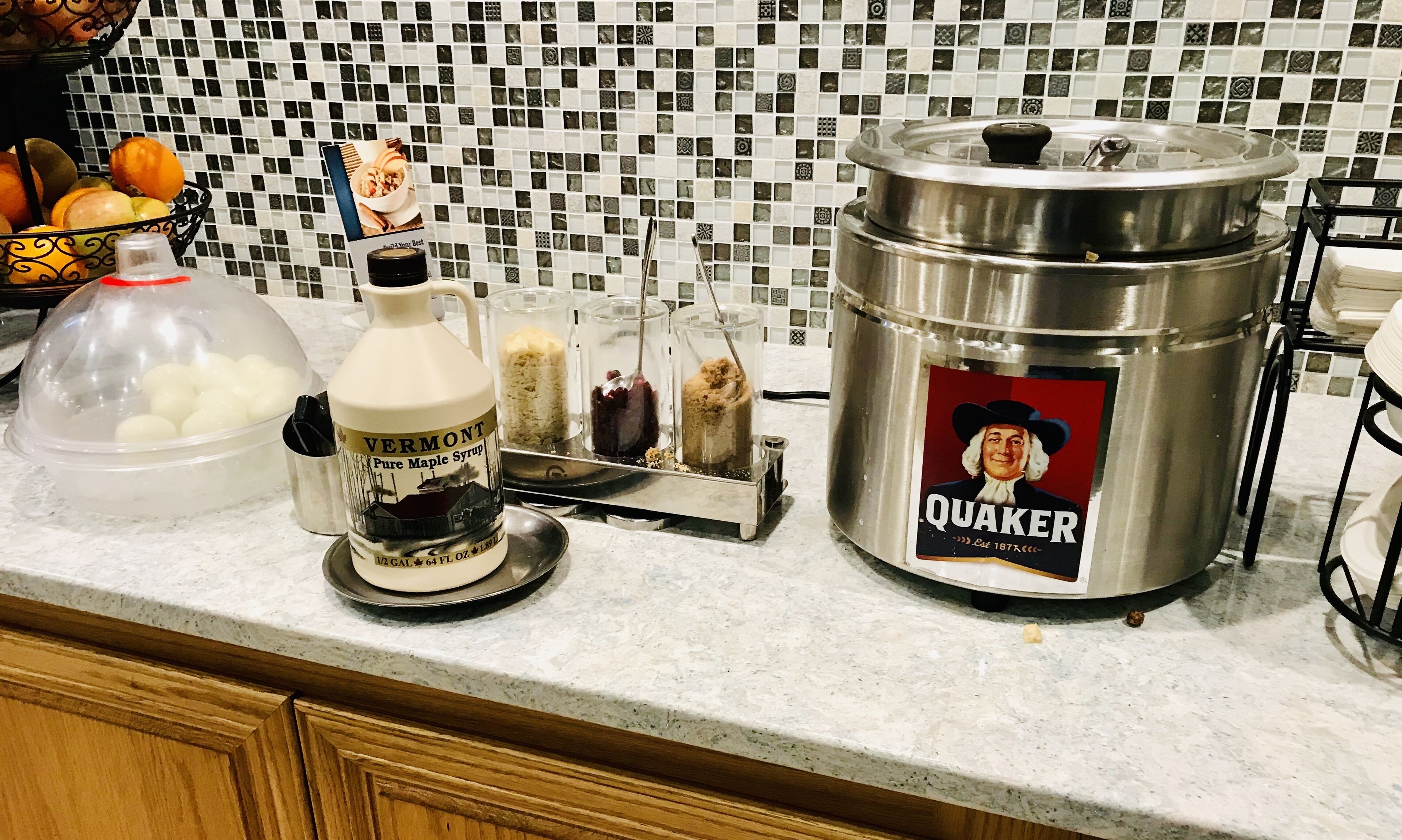 Una encimera de cocina con una olla metálica grande con la etiqueta "QUAKER" y un recipiente con la etiqueta "VERMONT Pure Maple Syrup".