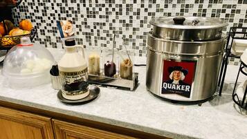 Una encimera de cocina con una olla metálica grande con la etiqueta "QUAKER" y un recipiente con la etiqueta "VERMONT Pure Maple Syrup".