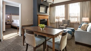 Habitación de hotel con una mesa de comedor, sillas, un sofá, una chimenea y un televisor montado en la pared.