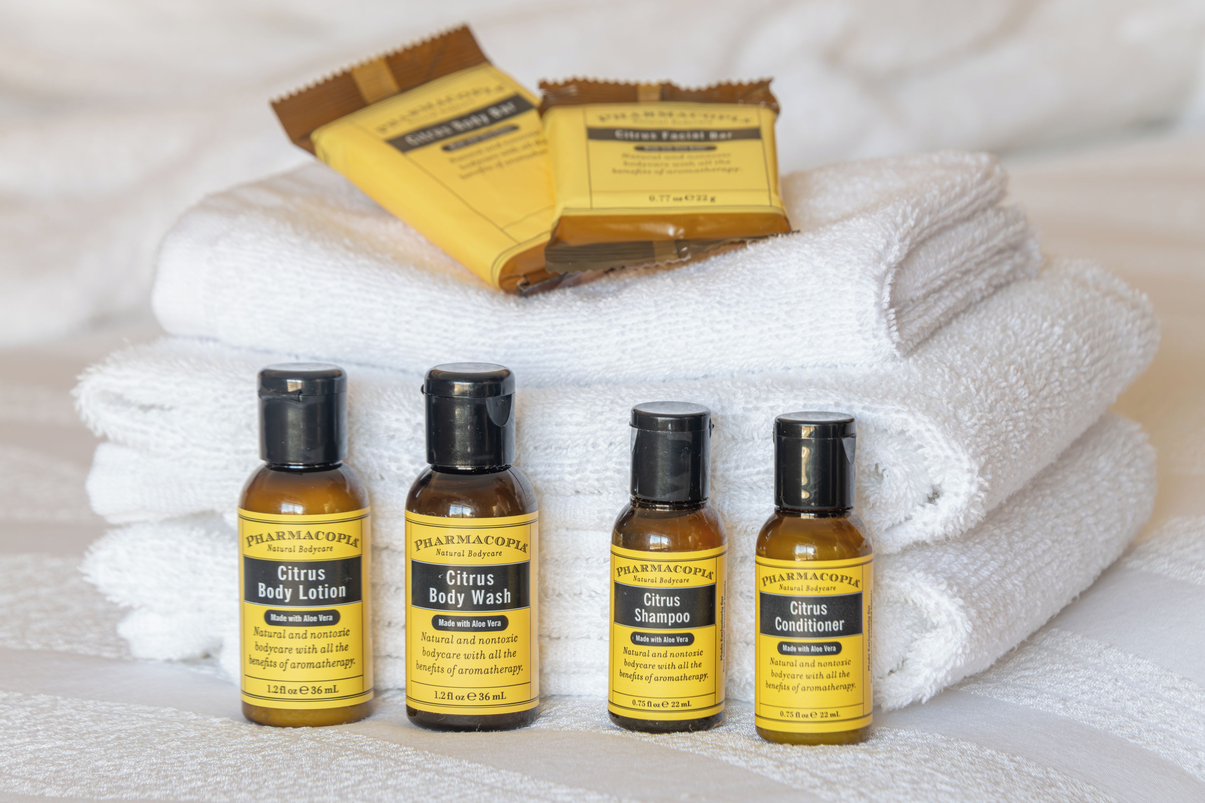 A set of toiletries including body lotion, body wash, shampoo, and conditioner, all labeled with 'PHARMACOPIA' and 'Made with Aloe Vera'.