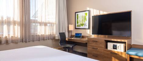 A hotel room with a large bed, a desk with a laptop, a television, and a microwave.