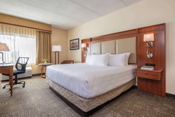 A hotel room with a large bed, a desk with a chair, a small table, and a lamp.