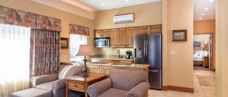 A modern kitchen with wooden cabinets, a stainless steel refrigerator, and a microwave. There is a dining area with a table and two armchairs.