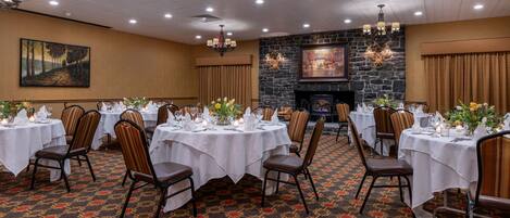 A banquet hall with multiple round tables set for dining, each with white tablecloths and floral centerpieces.