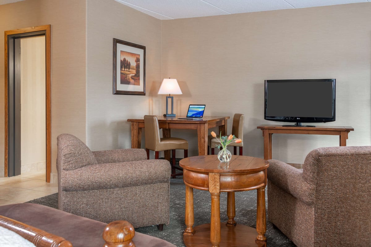 Une chambre d’hôtel dotée d’un coin salon comprenant deux canapés, une petite table ronde avec un vase, un bureau avec un ordinateur portable, une lampe et un téléviseur posé sur un meuble.