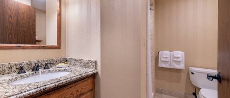 A bathroom with a granite countertop sink, wooden vanity, a mirror, and a toilet.