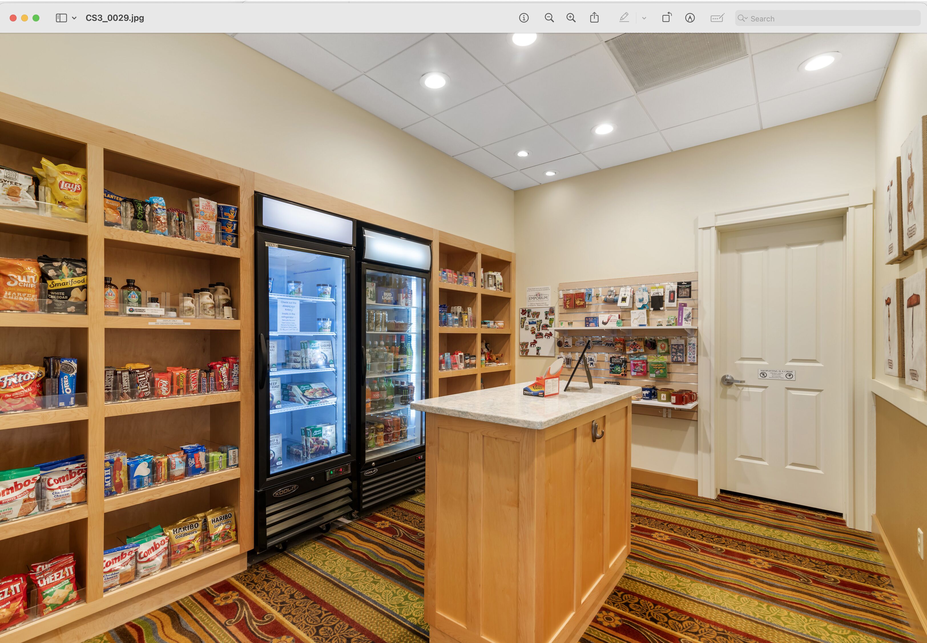 A hotel room with a kitchenette, a refrigerator, and a variety of food items on shelves.
