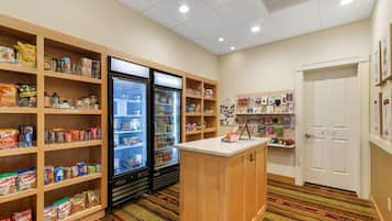 A hotel room with a kitchenette, a refrigerator, and a variety of food items on shelves.
