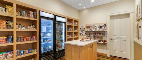 A hotel room with a kitchenette, a refrigerator, and a variety of food items on shelves.