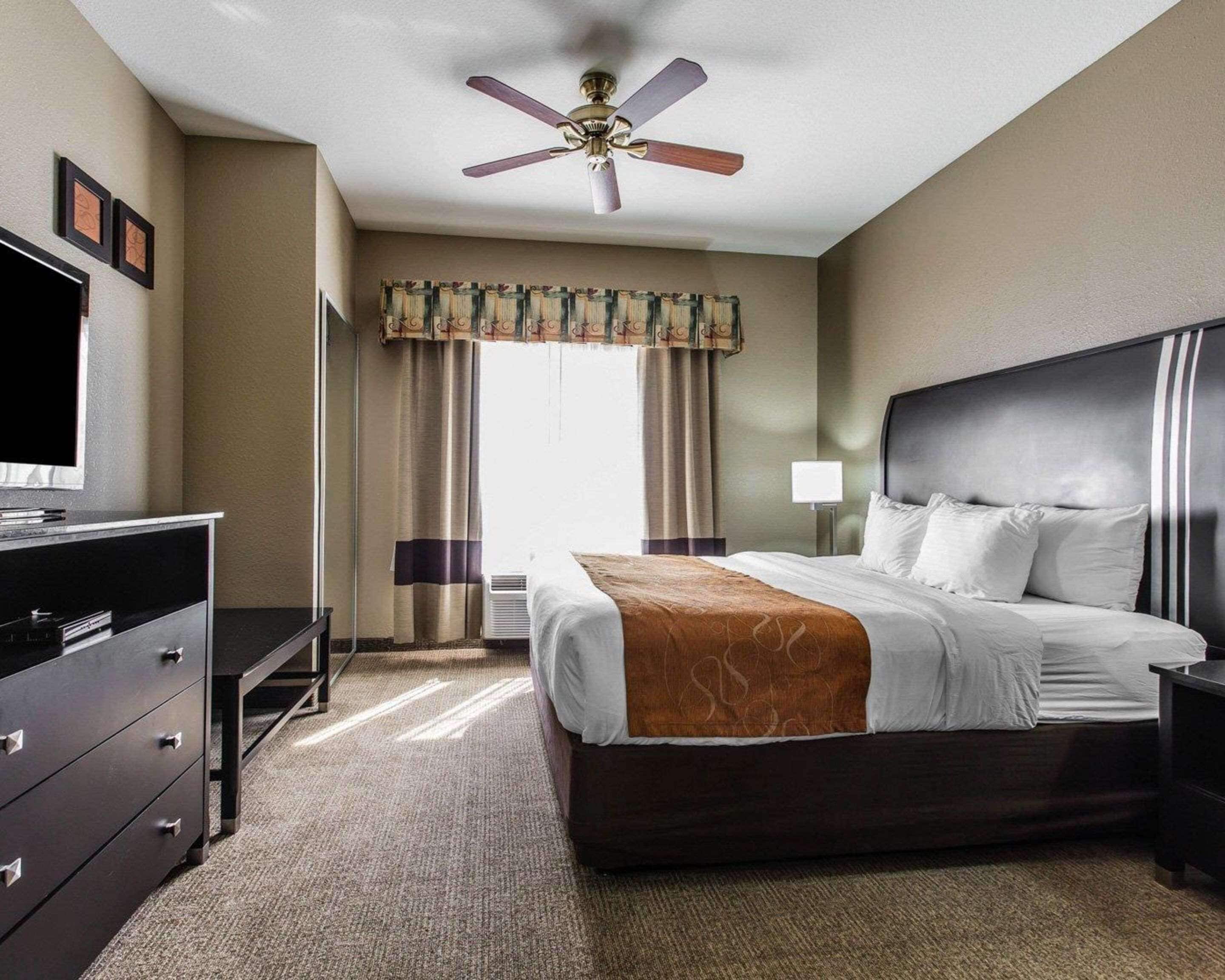 A hotel room with a bed, a desk, a television, and a ceiling fan.