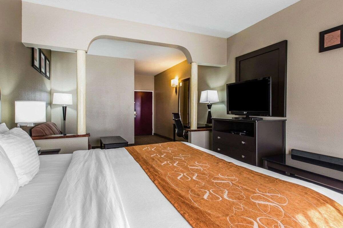 Ein Hotelzimmer mit einem Bett, einem Fernseher, einem Schreibtisch mit Lampe und einem Sessel.