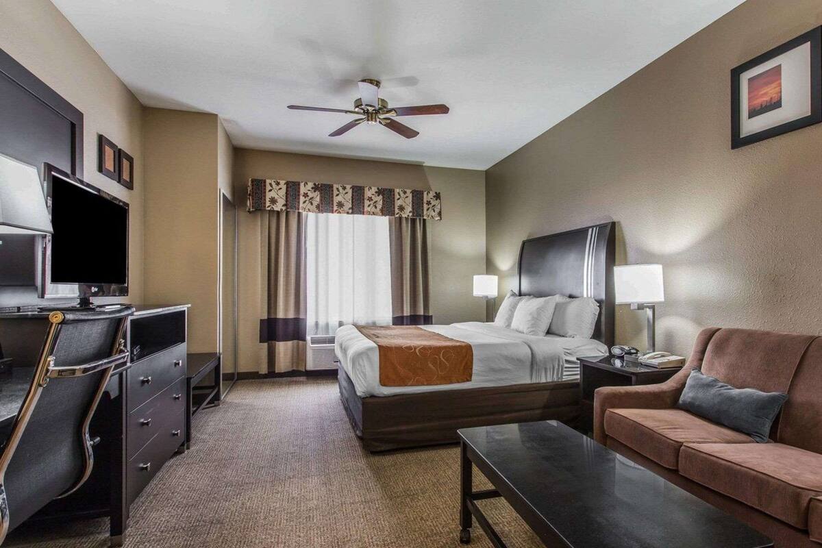 A hotel room with a bed, a desk with a TV, a ceiling fan, a sofa, and a coffee table.