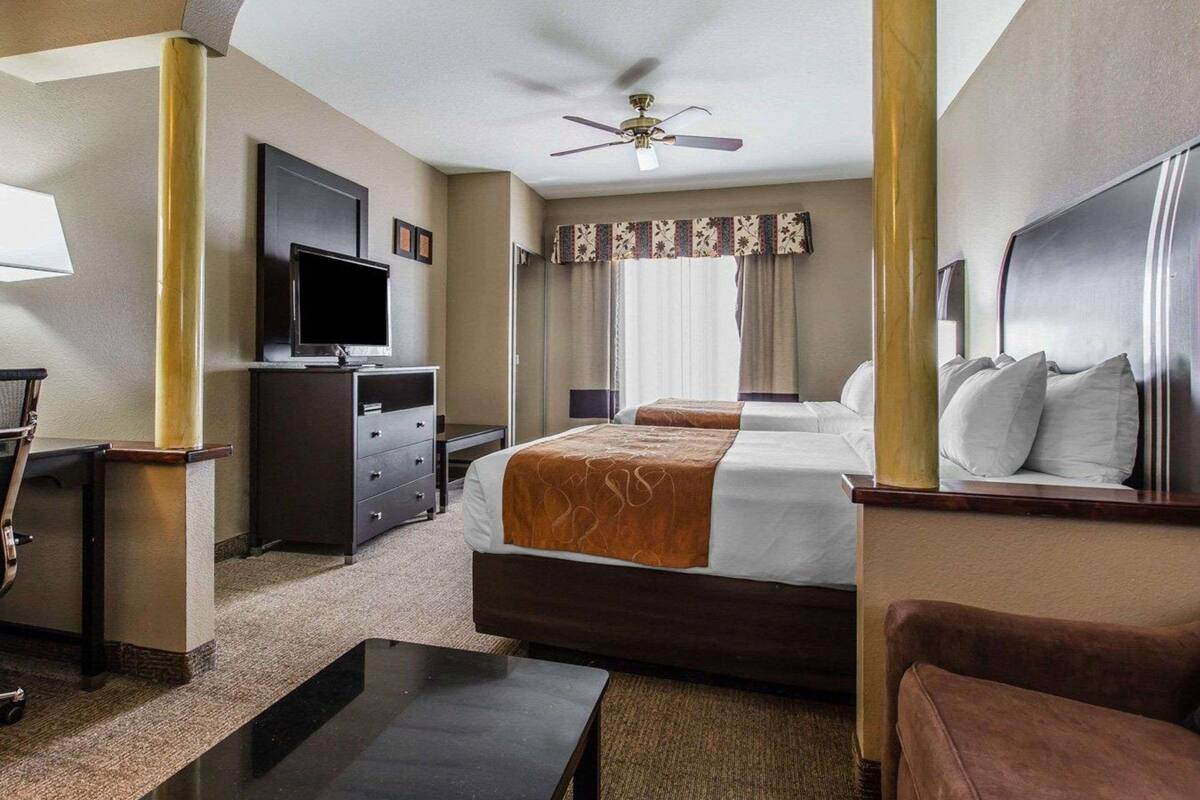 A hotel room with a bed, a desk, a television, a ceiling fan, and a window with curtains.