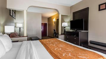 A hotel room with a large bed, a flat-screen TV, a desk with a lamp, and a chair.