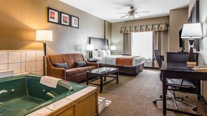A hotel room with a bed, a sofa, a desk, a chair, a coffee table, a TV, a ceiling fan, and a bathtub.