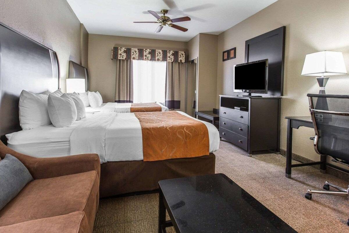 A hotel room with two beds, a desk, a chair, a television, and a ceiling fan.