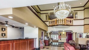 A hotel lobby with a reception desk, a chandelier, a sofa, and a staircase.