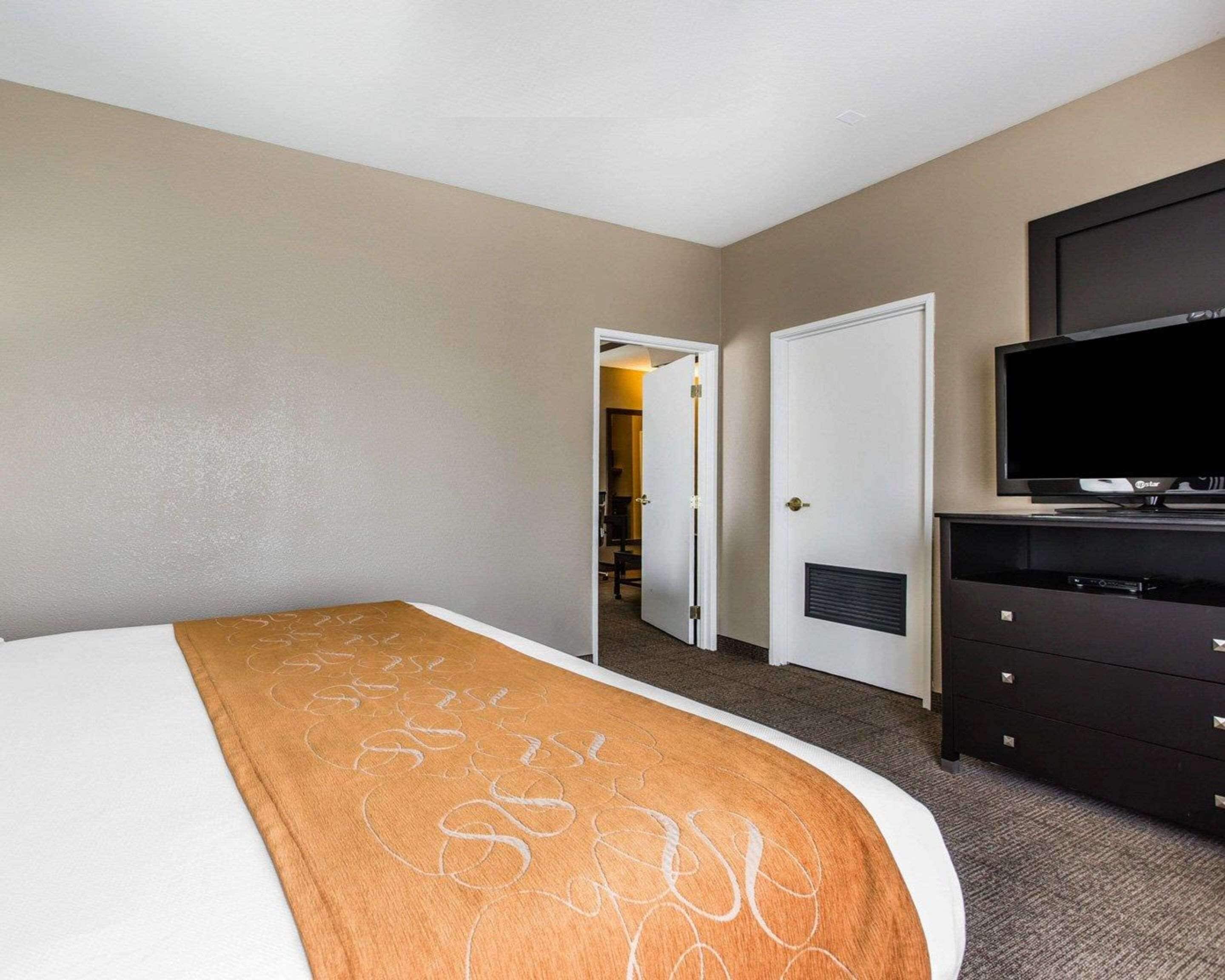 A hotel room with a bed, a television, a dresser, and a door leading to a hallway.