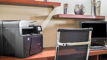 A desk with a printer, a laptop, and a chair. There are decorative vases on a shelf above the desk.