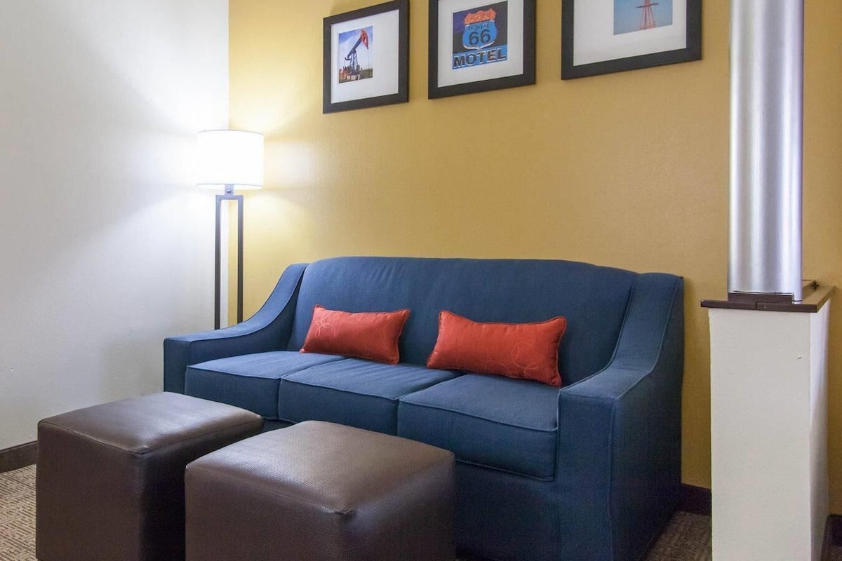 A blue sofa with two red cushions, two brown ottomans, a floor lamp, and three framed pictures on the wall.