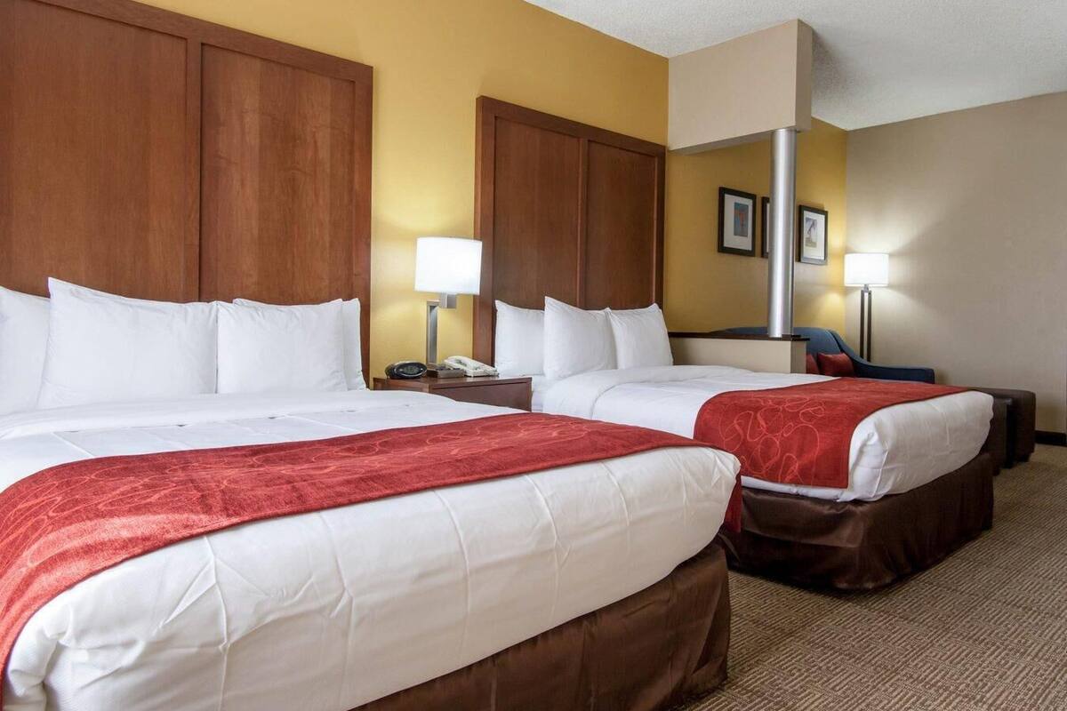 A hotel room with two beds, wooden headboards, a beige carpet, and a yellow accent wall.