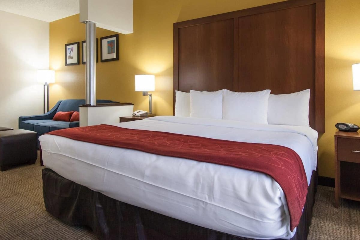 A hotel room with a large bed, a desk, a chair, and a lamp.