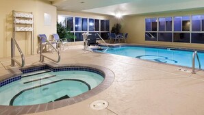 An indoor swimming pool with a hot tub, lounge chairs, and a towel rack.