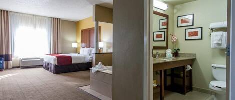 A hotel room with a bed, a desk, a chair, a bathroom with a toilet, a sink, and a mirror.