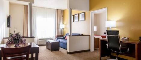 A hotel room with a dining table, a sofa, a desk with a chair, and a bed.