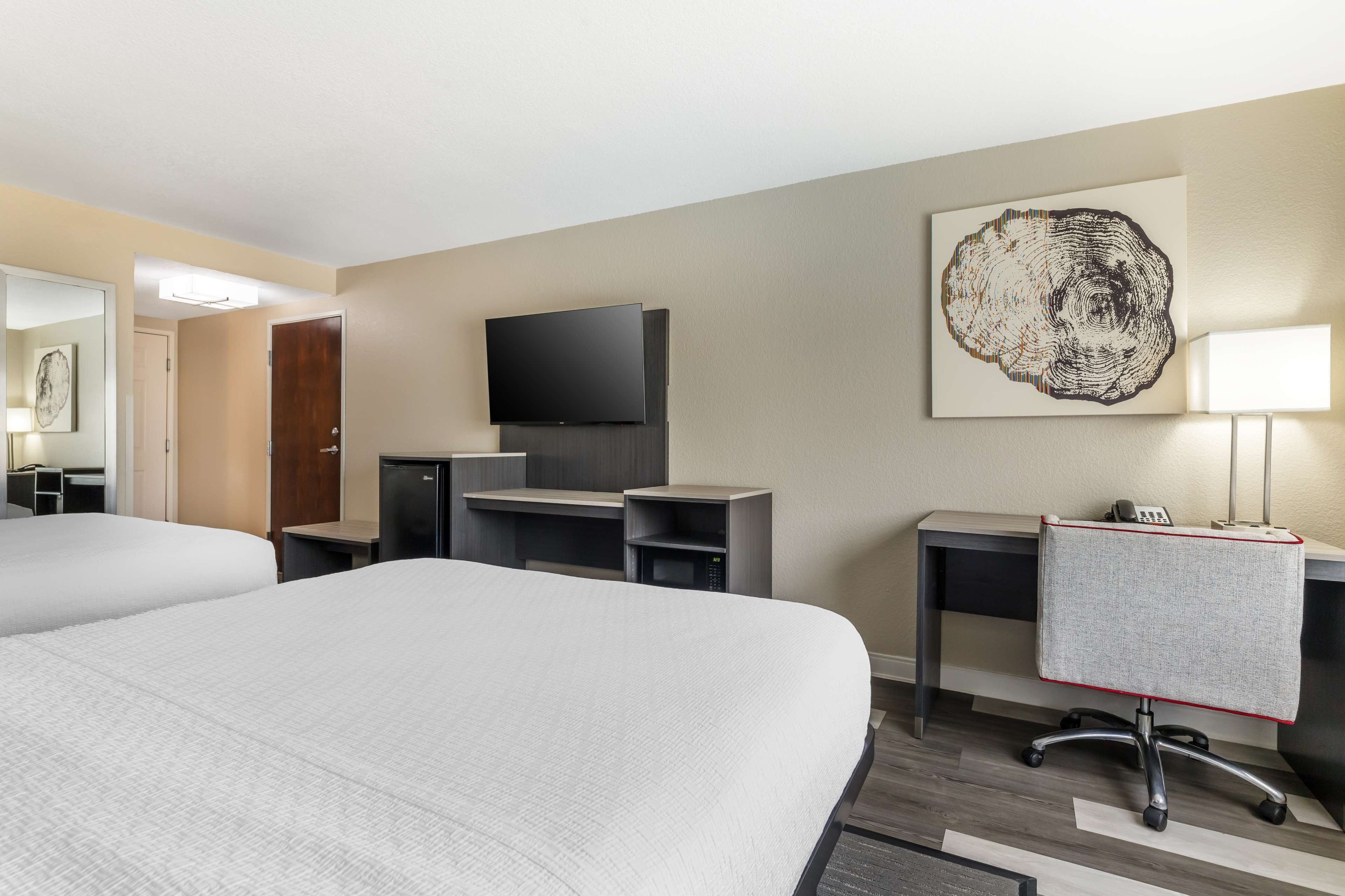 Habitación de hotel con dos camas, un escritorio con computadora, televisión y una obra de arte en la pared.