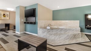 A modern bathroom with a marble sink, a flat-screen TV mounted on the wall, and a wooden bench. - Best Western Prime Inn & Suites (Poteau)