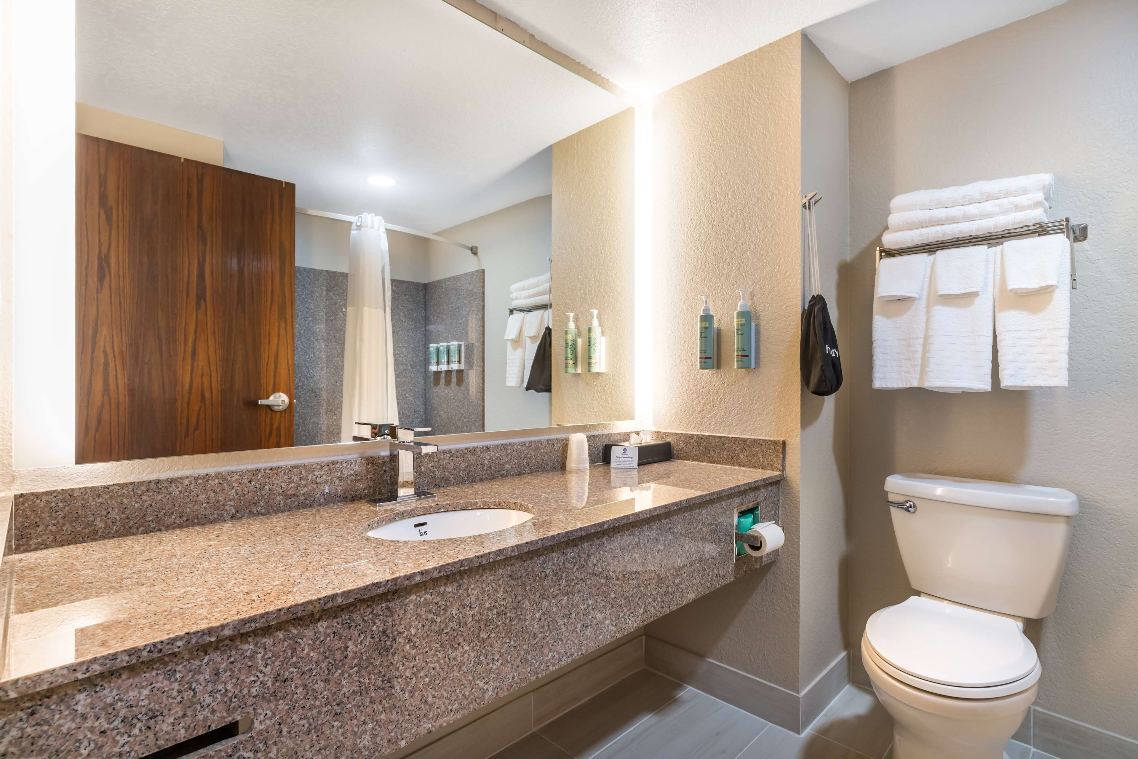 A bathroom with a granite countertop, two sinks, a toilet, and a towel rack with folded towels.