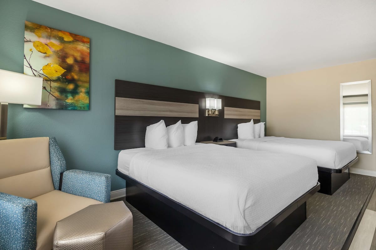 Quarto de hotel com duas camas, um sofá, um quadro e uma mesa de cabeceira com abajur.