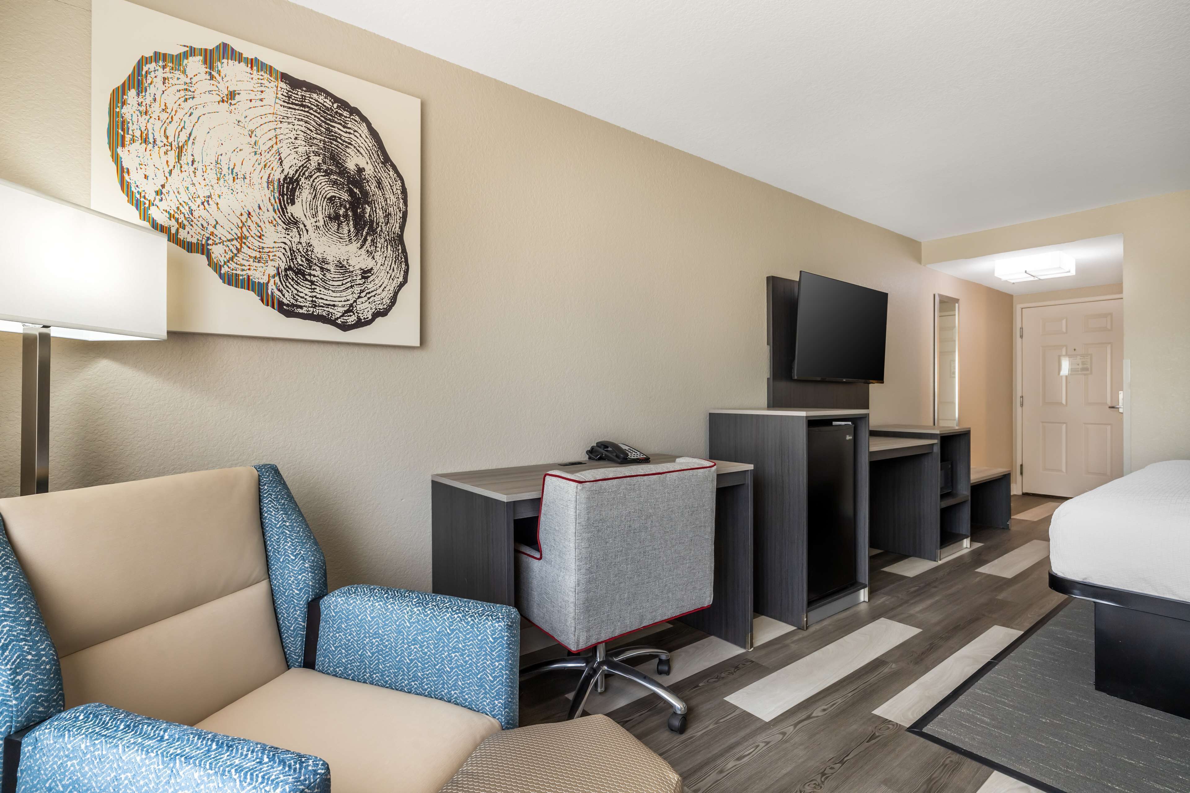 Habitación de hotel con cama, escritorio con silla, televisor y una gran obra de arte abstracta en la pared.