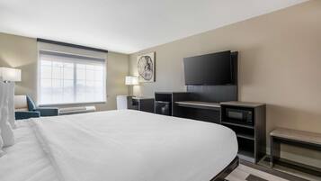 A hotel room with a large bed, a flat-screen TV, a microwave, and a desk with a lamp.