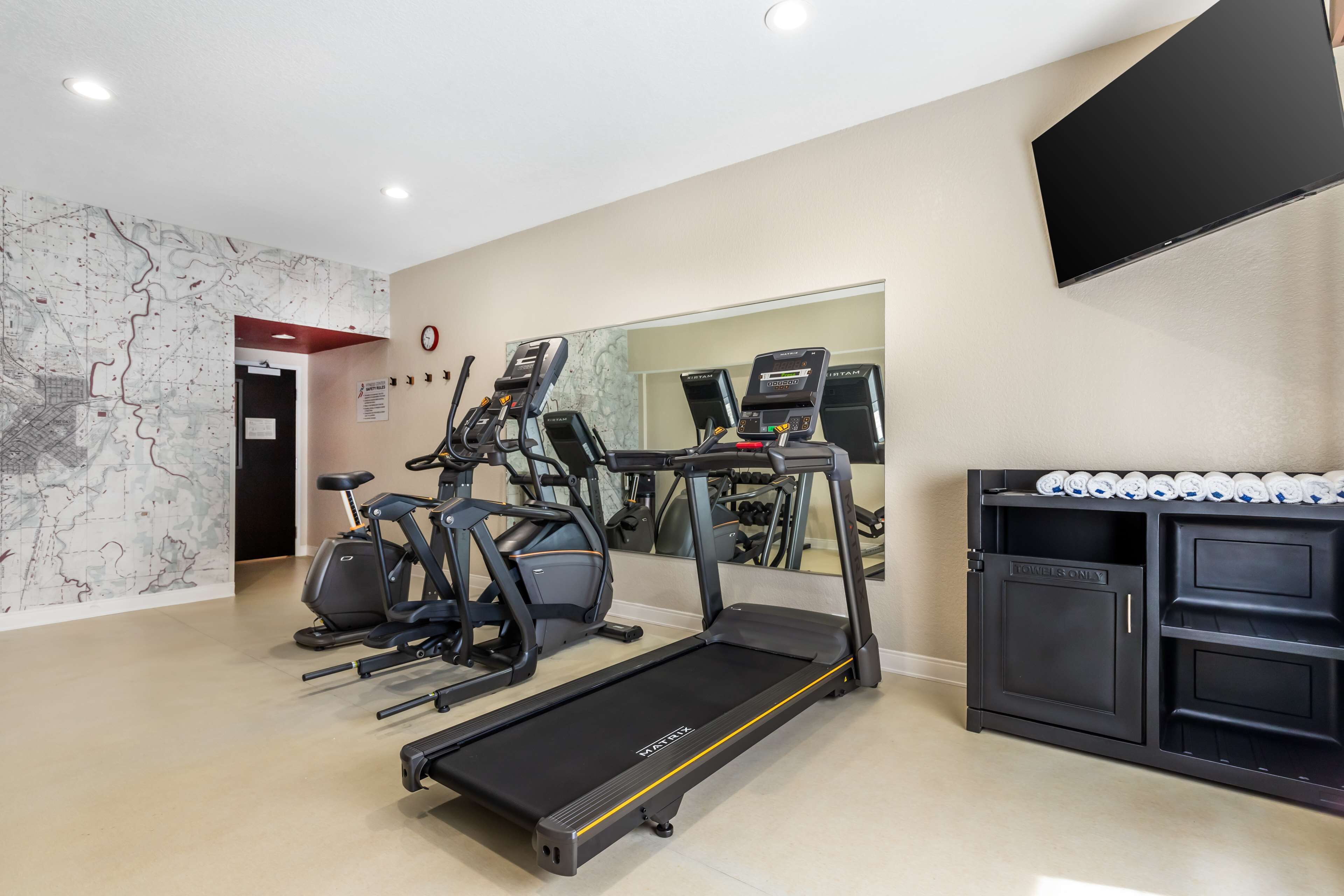 A gym with treadmills, elliptical machines, and a mirrored wall.