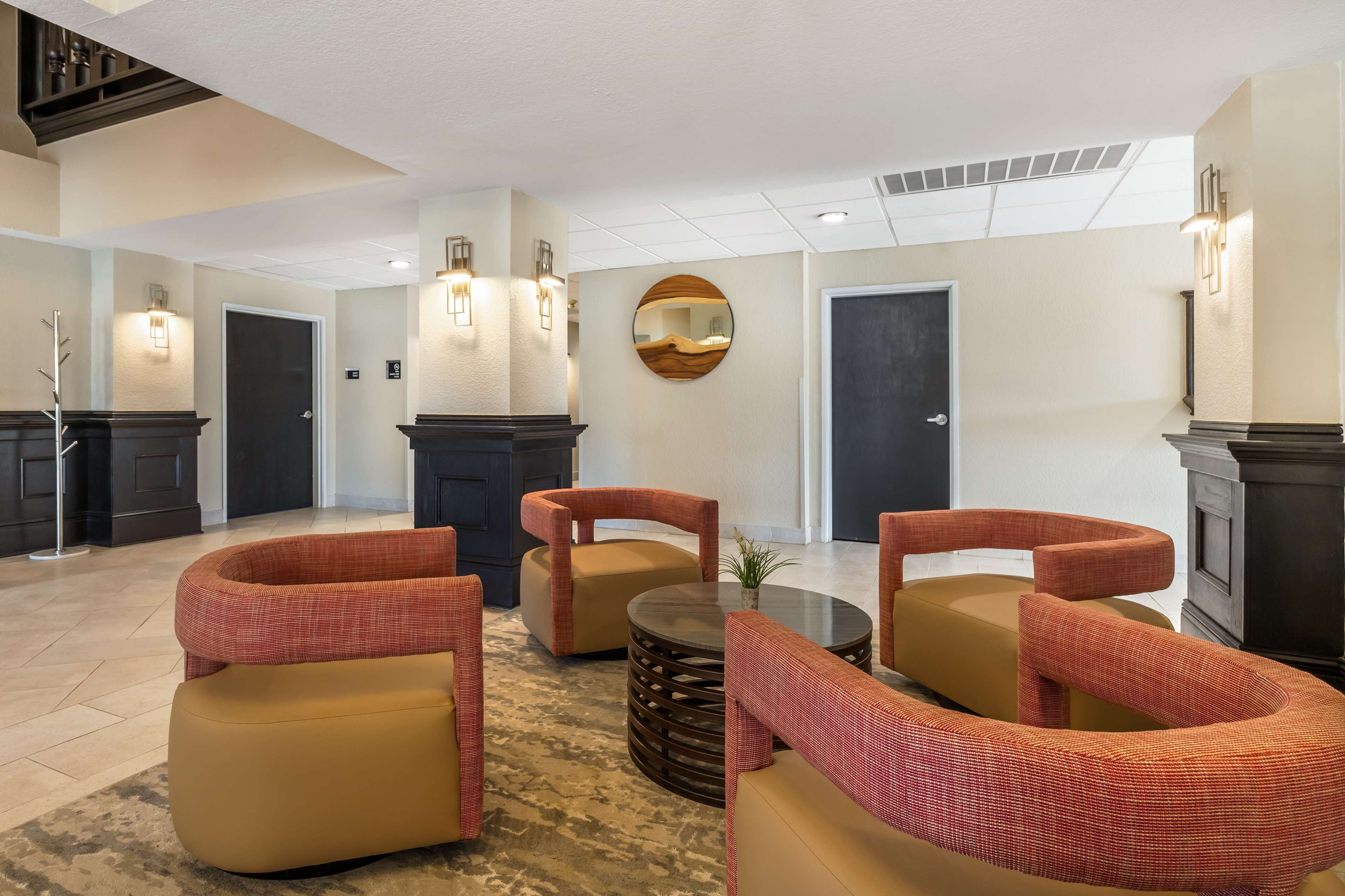Un vestíbulo con diseño moderno, que incluye una zona de estar con sofás y sillones, una mesa redonda y un espejo decorativo.