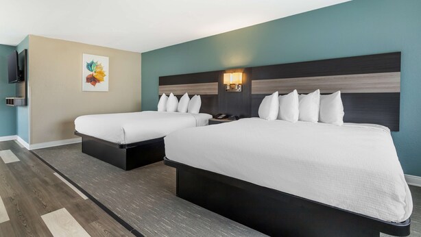 A hotel room with two beds, a TV, a painting, and a nightstand with a lamp.
