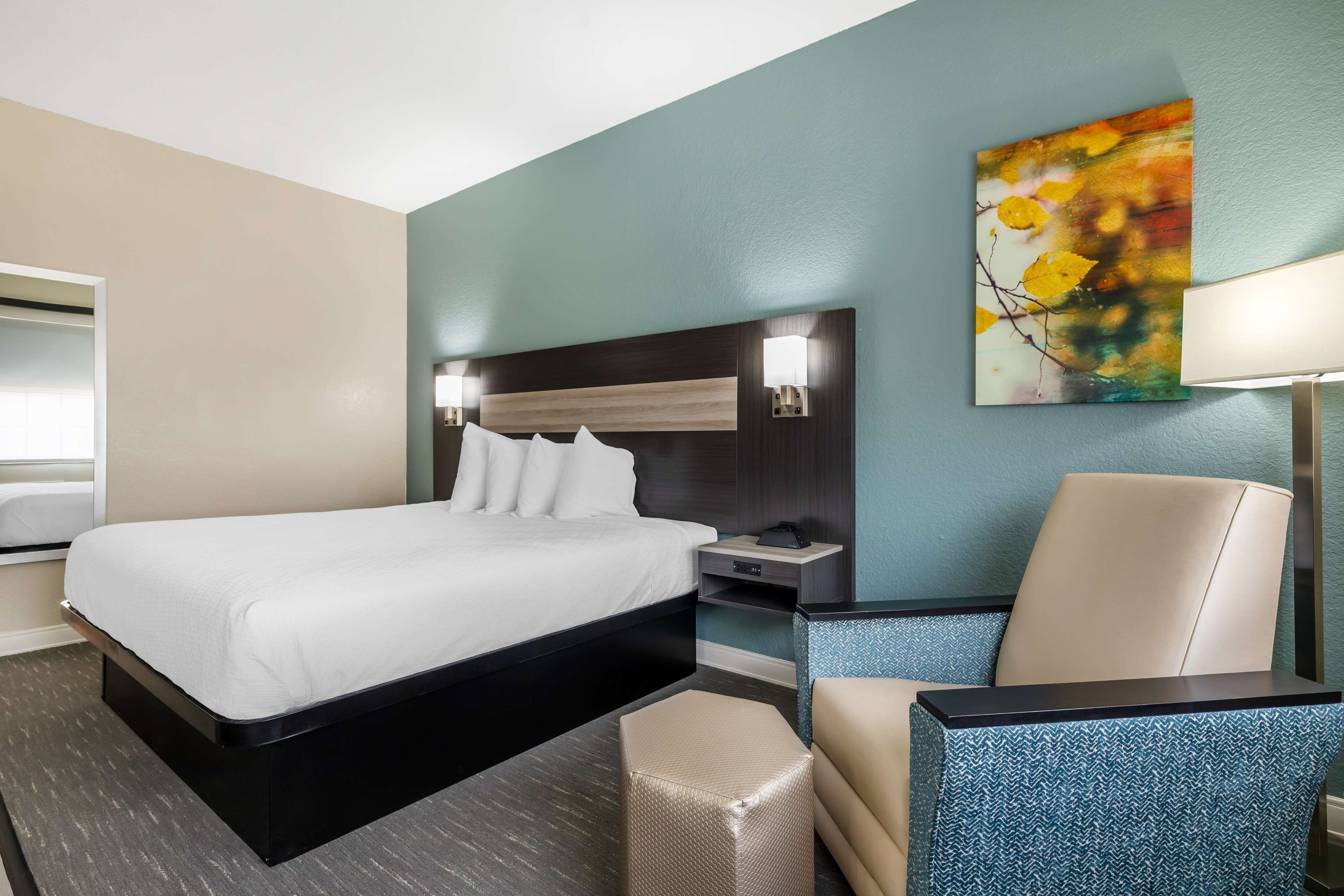 A hotel room with a large bed, a desk with a chair, a nightstand, and a painting on the wall.