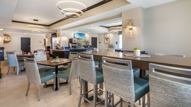 A modern dining area with high tables and chairs, a kitchen in the background, and pendant lighting. - Best Western Prime Inn & Suites (Poteau)