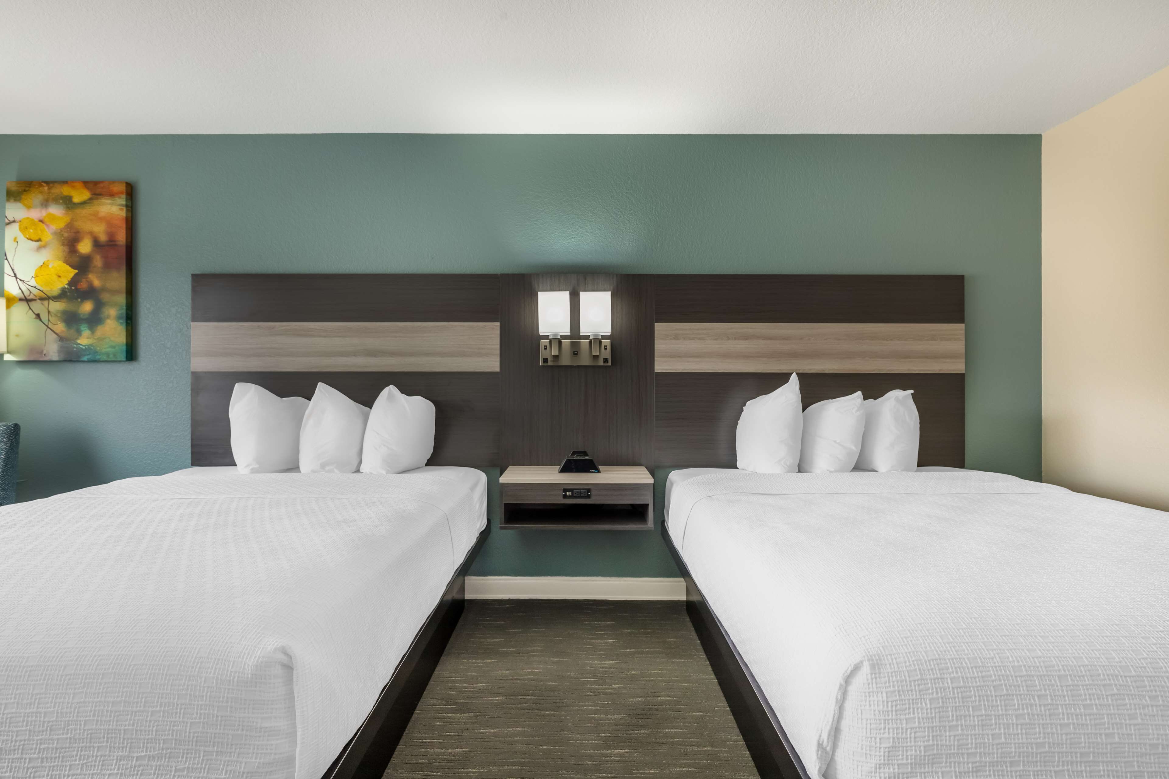 Ein Hotelzimmer mit zwei Betten, einem Nachttisch, einem Gemälde und einer Wandleuchte.