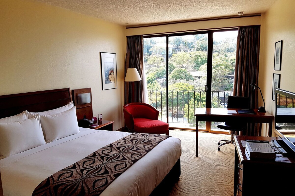 A hotel room with a bed, a desk, a chair, a TV, and a balcony with a view.