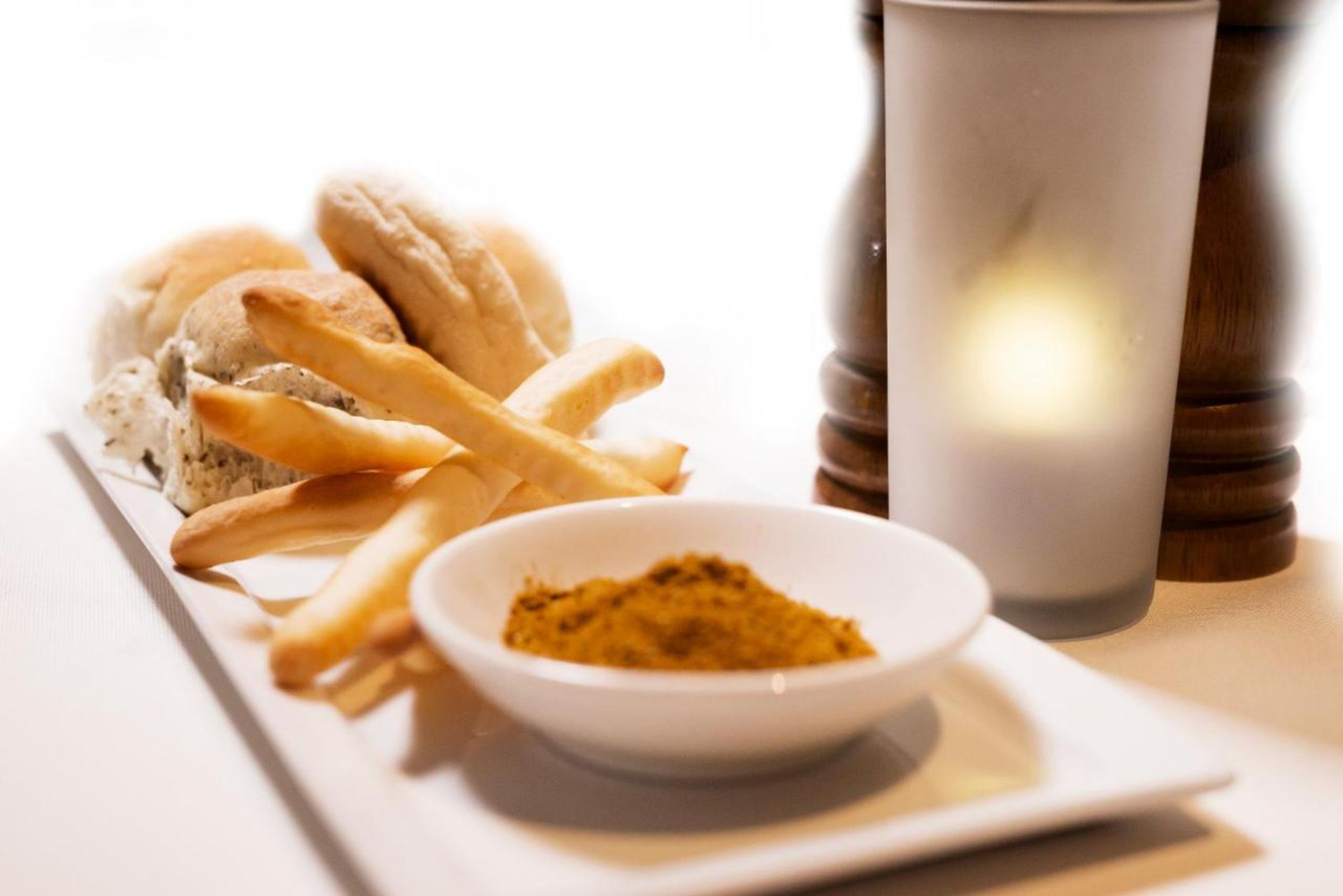 Un plato con papas fritas, un cuenco de mostaza y un salero sobre una mesa blanca.