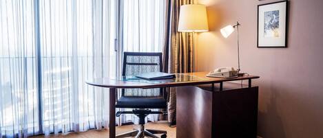 Habitación de hotel con escritorio, silla, lámpara y dos cuadros en la pared.