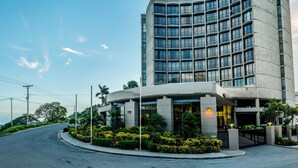 Un hôtel moderne à la façade incurvée, doté de nombreux balcons et d’un espace d’entrée aménagé.