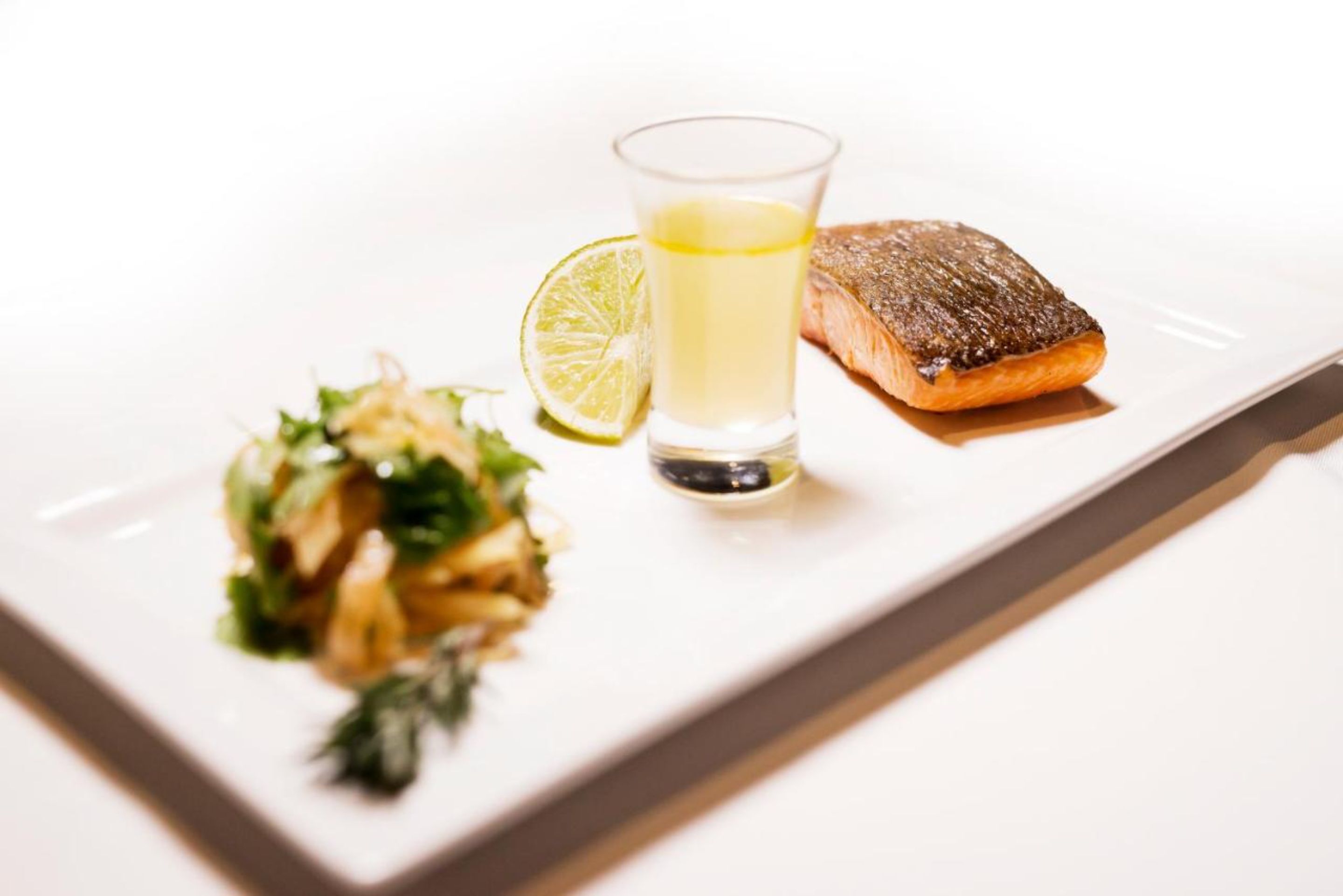 A plate with grilled salmon, a glass of lemon juice, and a side salad.