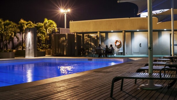 Une piscine nocturne dotée d’une terrasse en bois et de chaises longues.